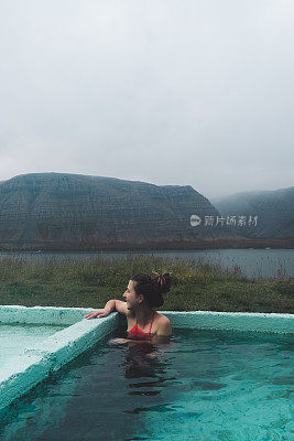 在冰岛的峡湾景色中，一个女人在热水池里洗澡