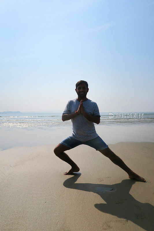 印度男子练习侧弓步(Skandasana)瑜伽姿势在潮湿的沙滩上，水的边缘，Palolem海滩，果阿，印度