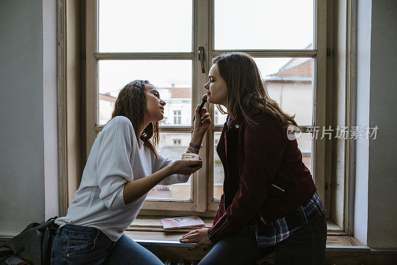 两个十几岁的女孩在靠近窗户的教室里化妆