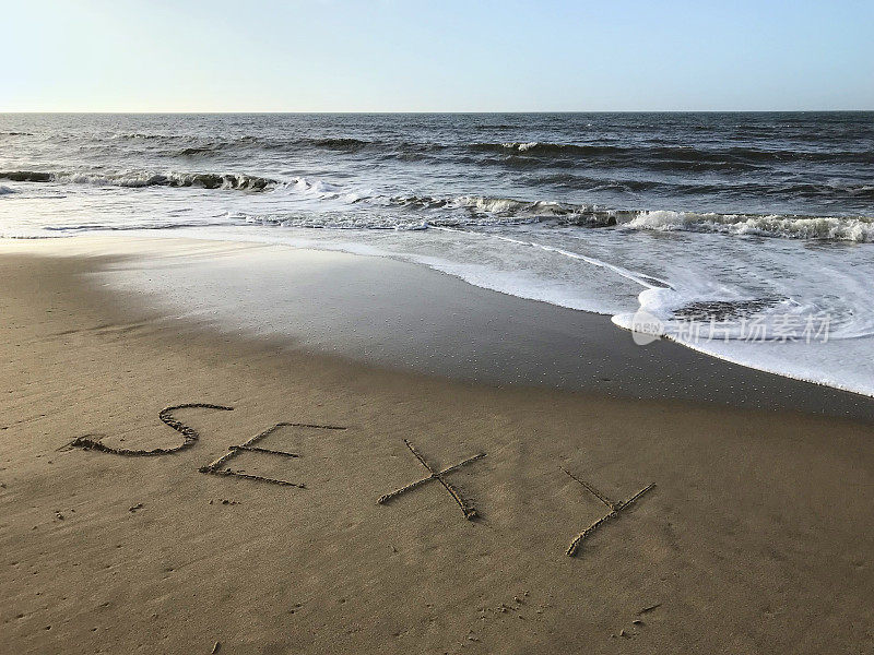 图片写在阳光沙滩上，性感的词写在沙子上，用木棍，海浪，概念社交媒体照片在柔软的金色沙滩上书写字母，多塞特，英国海边的海岸线