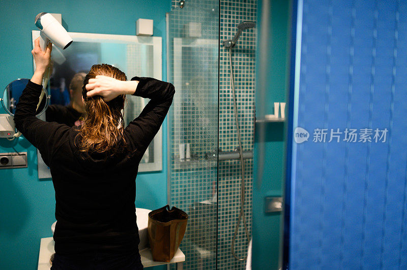 金发女人在浴室里用吹风机梳理和烘干头发