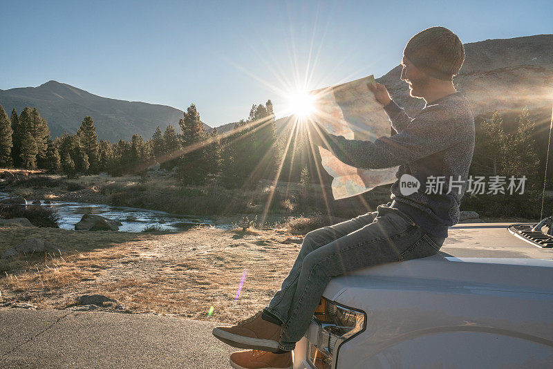 公路旅行概念;一名男子坐在汽车引擎盖上，在地图上查看方向