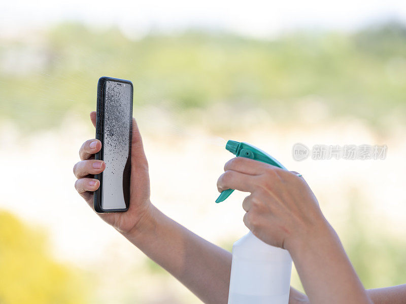 女人在智能手机上喷洒消毒剂