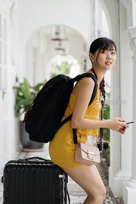 年轻的亚洲女性游客背包和行李使用智能手机查看地图或拼车服务