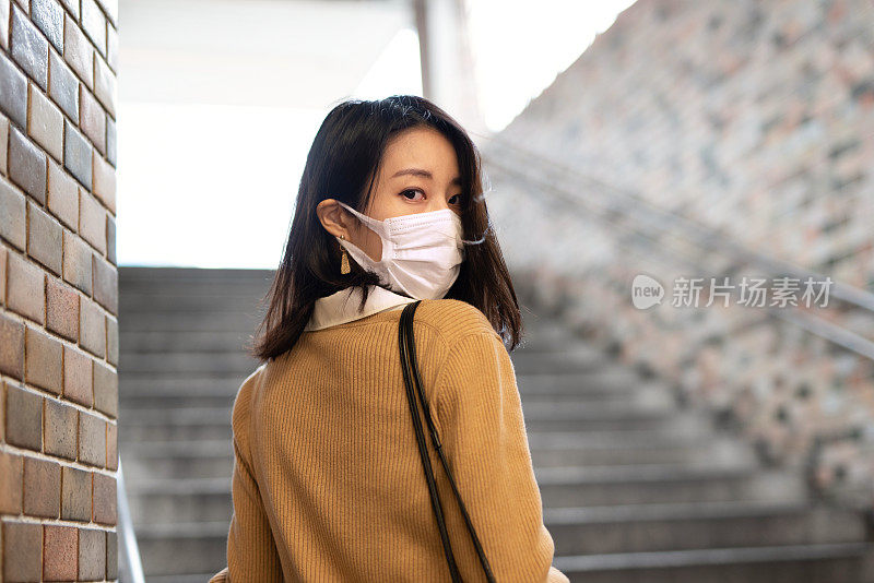 年轻的亚洲女子戴着面具回头看楼梯