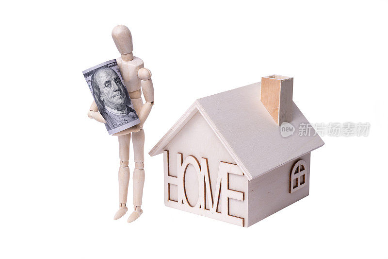 孤立的木制简单的玩具房子和一个象征性的人在白色背景上的木制雕像，拿着一张卷起来的100美元钞票