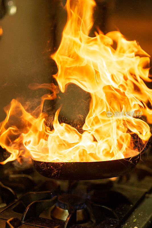 厨师在商用厨房炉子上用平底锅用火焰烹饪