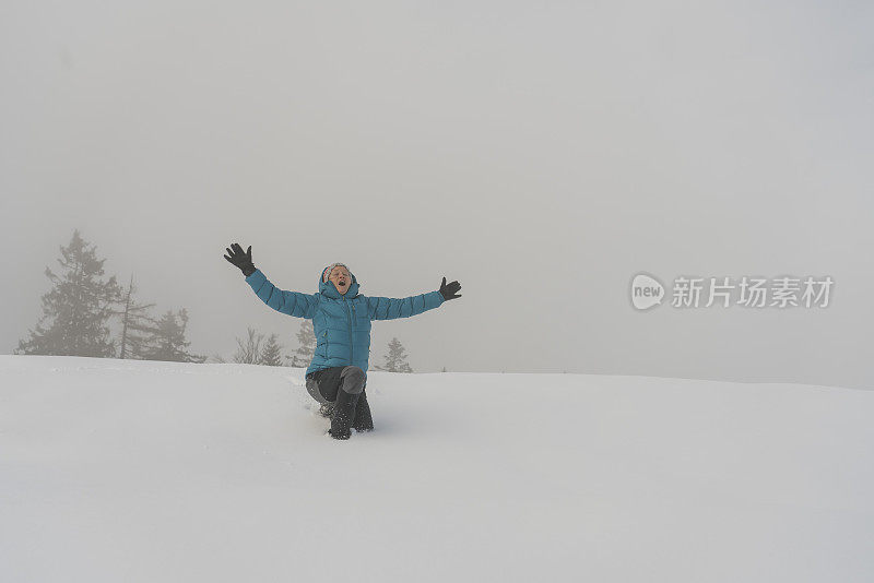 成熟的女人穿着皮大衣，跪在雪地里，对着天空