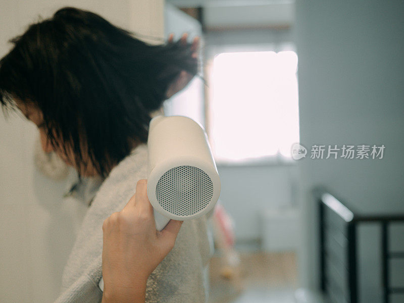 亚洲女性干燥她的头发与一个吹风机。