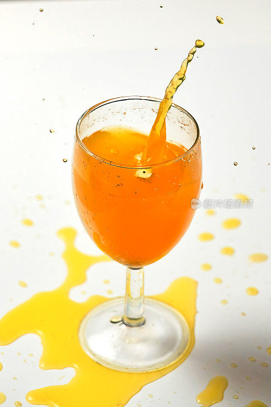 一颗骰子掉进了一杯橙色液体中，引起了水花四溅。特写白色背景