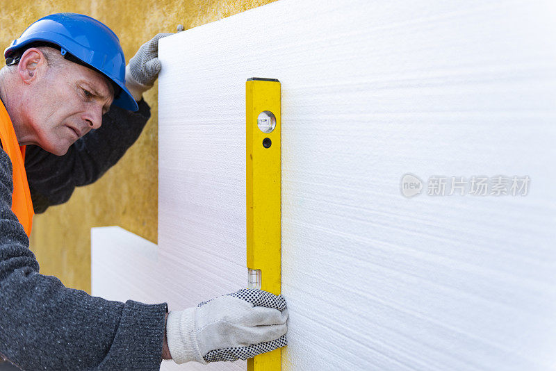 建筑工人在建筑工地的墙壁上放置聚苯乙烯保温板