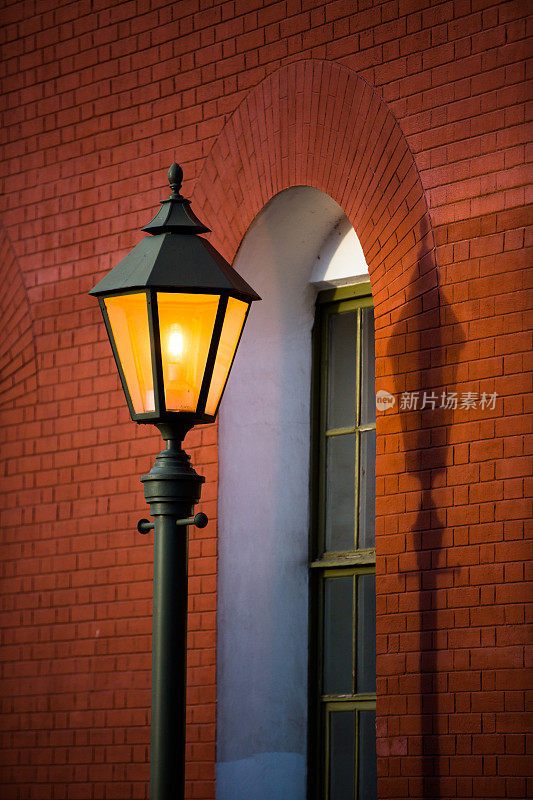 街灯发出的橙色灯光。红色砖墙旁闪烁着古老的街灯