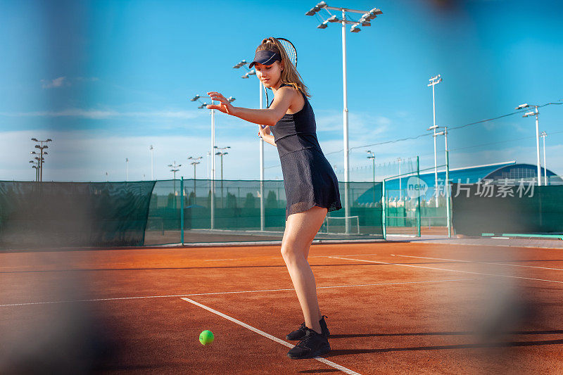 一个漂亮的女人在球场上打网球。阳光、培训的竞争。户外运动，团队合作。积极的生活方式，拿着球拍和球的运动员。扔球
