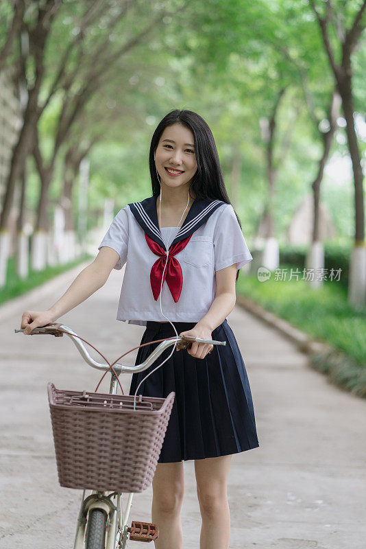 年轻的亚洲女大学生，推着自行车，面带微笑