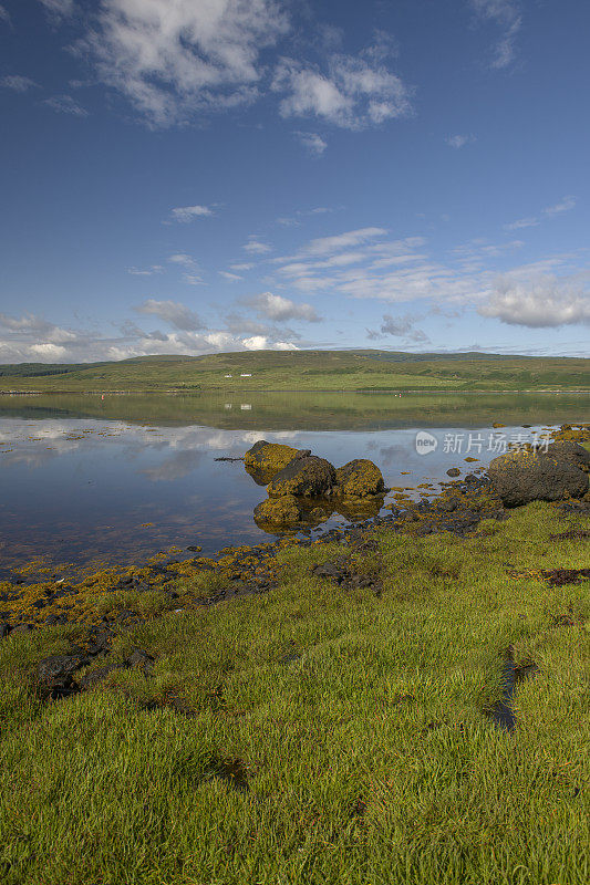苏格兰斯凯岛格林肖尼什湖的长满草的岸边，水中有岩石和倒影。