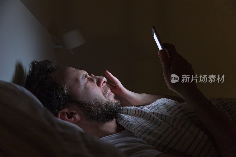 成年困倦的男人半夜醒来在床上上网，无法入睡