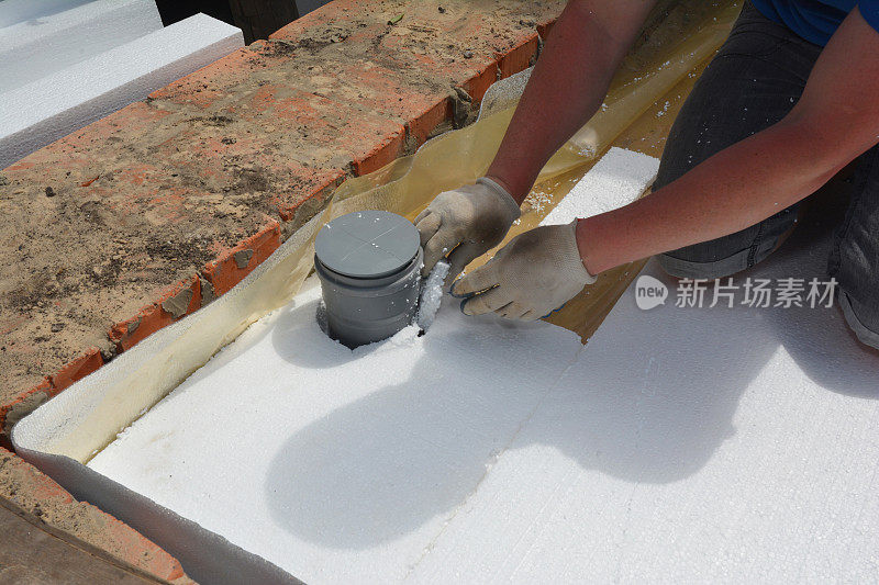 浴室的隔热地板。一家建筑承包商正在防水膜上安装硬质泡沫板保温材料，防水膜切割下水道管道的边缘。