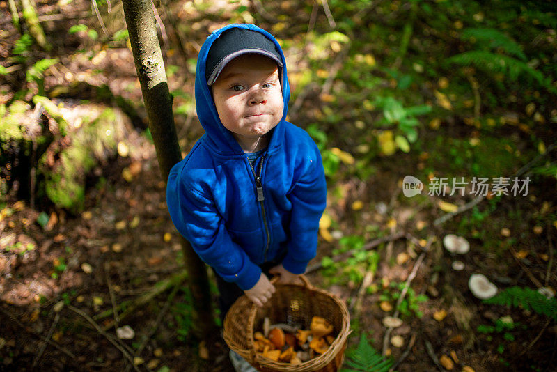 在森林里拿着一篮蘑菇做鬼脸的滑稽男孩