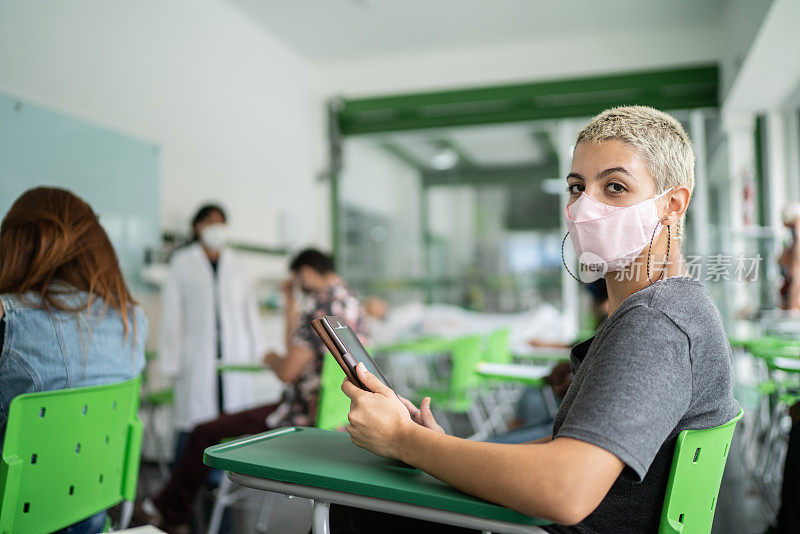 一名女学生在教室里使用数码平板电脑的肖像——使用口罩