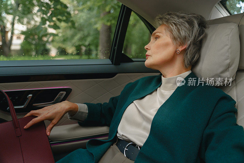 一位优雅的老妇坐在真皮内饰的商务舱的乘客座位上，她看着车窗外，我们看到后面是绿色的树木。