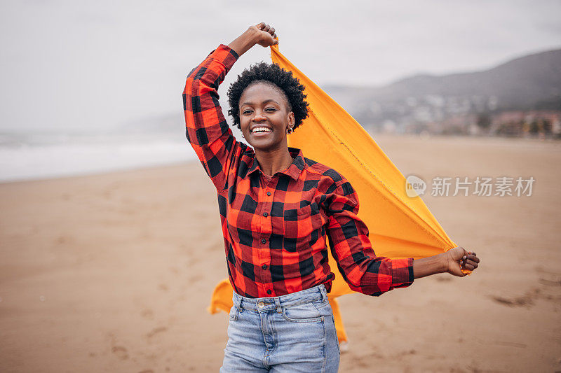 年轻女子在海滩上跑步，在风中有围巾的乐趣