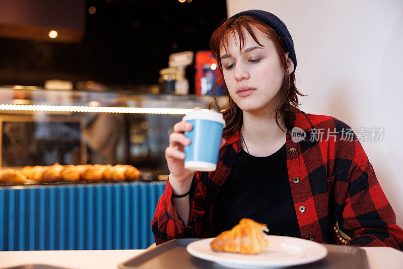 十几岁的女孩坐在小卖部前，用纸杯和糕点喝咖啡