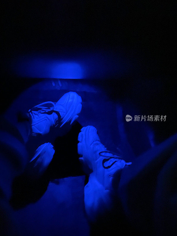 黑暗中，一个穿着白色运动鞋的年轻人的脚在桌子下面