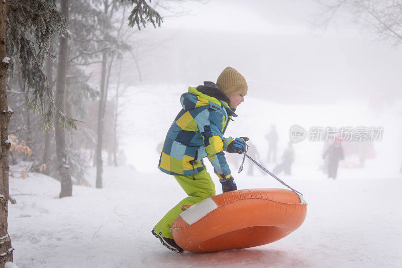 小男孩在雪管上从山上滑下来。