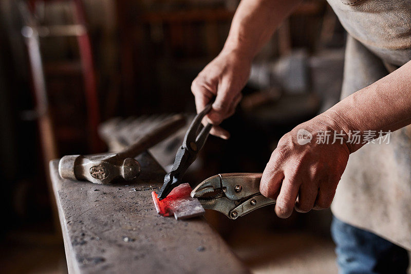 手，工具和金属与一名铁匠工作在制造或工业工厂的设计或工艺。有一名男性工人在铸造厂或锻炉从事金属加工的车间、创意和工业