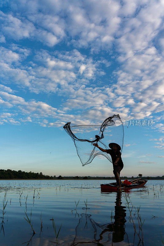 亚洲乡村的生活方式，一个戴着圆锥形帽子的当地男性渔民在黎明时分的淡水湖上划着木船