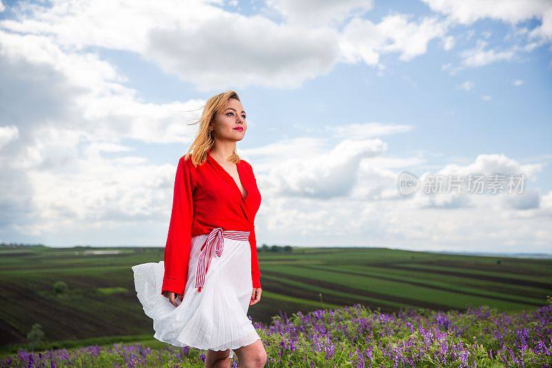 漂亮的金发女孩在一件红衬衫和红衬衫后面的花在田野里
