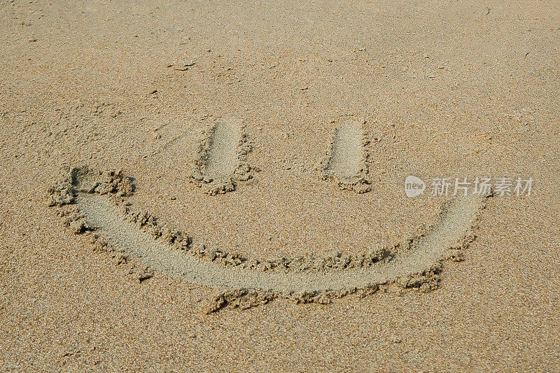 在阳光明媚的海滩上用木棍在潮湿的沙子上绘制笑脸的特写图像，高架视图，专注于前景，假期和度假概念