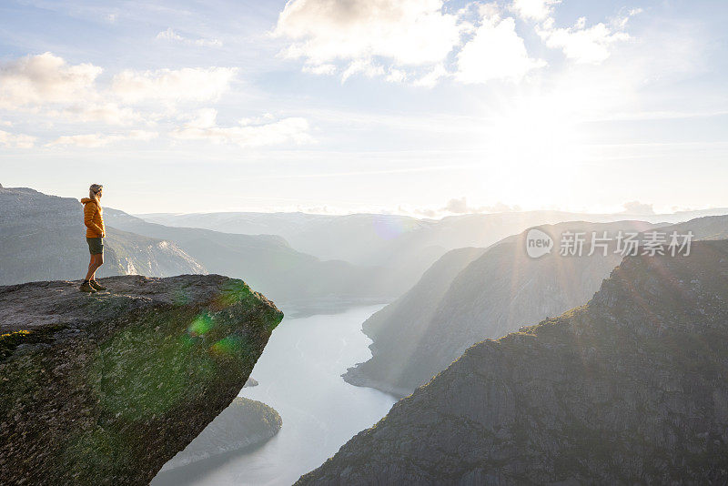 一名女徒步旅行者站在巨魔之舌(trollltunga)著名的岩石上，俯瞰湖面上的山谷全景，是挪威著名的探险之旅