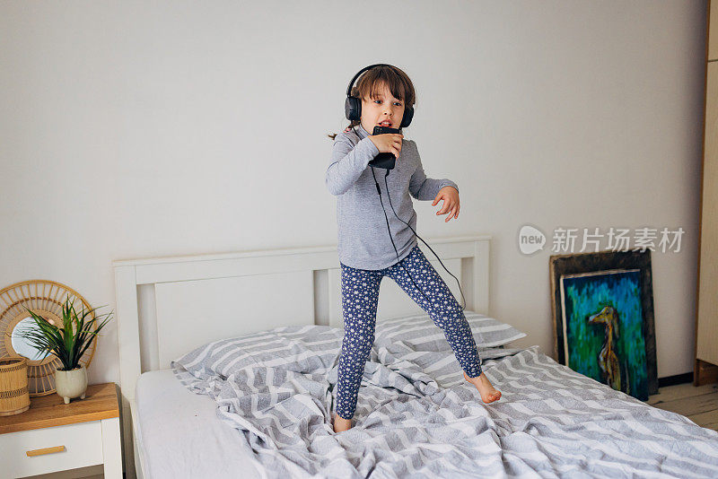 活泼的小女孩穿着睡衣在家里唱歌和听音乐