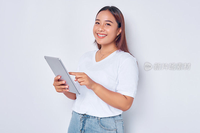 肖像微笑年轻的亚洲女孩在白色t恤使用数字平板隔离在白色背景