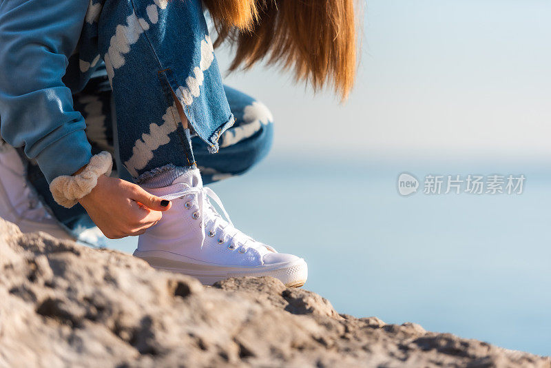 十几岁的女孩在一个阳光明媚的冬日在海边系白色运动鞋