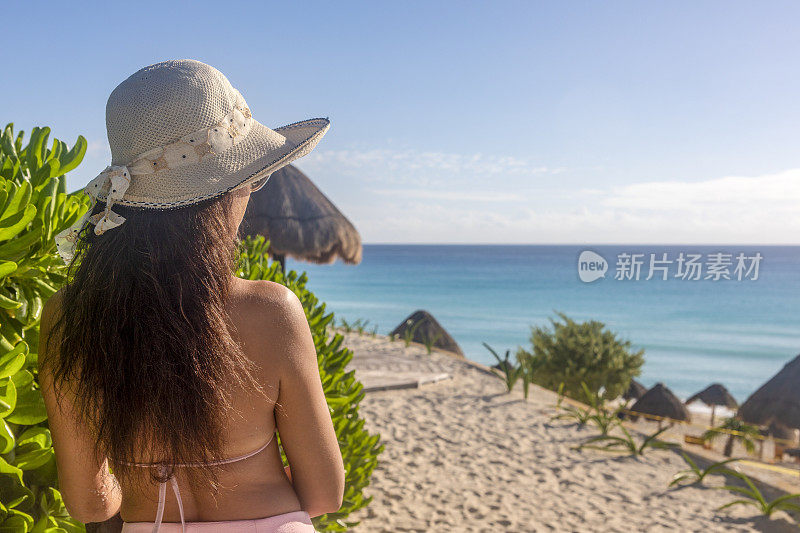 一个阳光明媚的日子，墨西哥坎昆的酒店区，海豚海滩上戴着帽子的性感女人。这是一个热带天堂般的海滩，白色和金色的加勒比海沙滩，非常受游客欢迎。