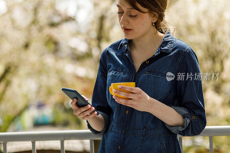 年轻女子站在阳台上，一边喝咖啡一边打电话