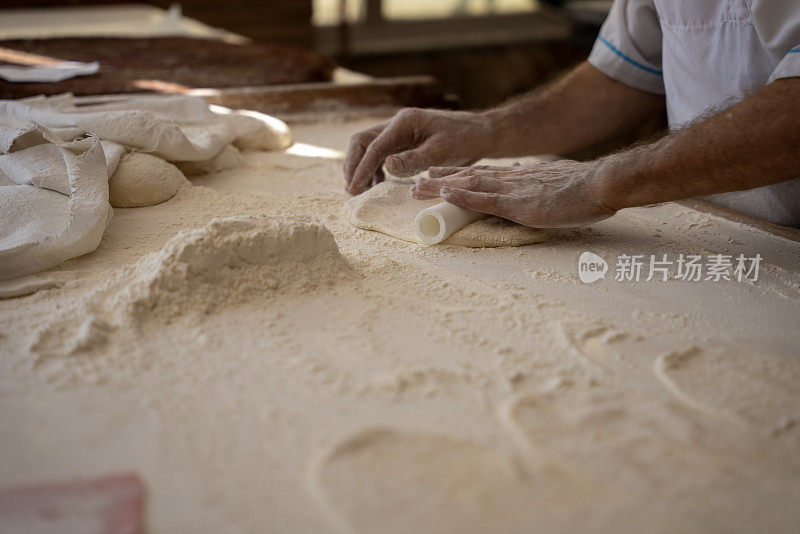 一个老人在面包店做面包，把面团铺好