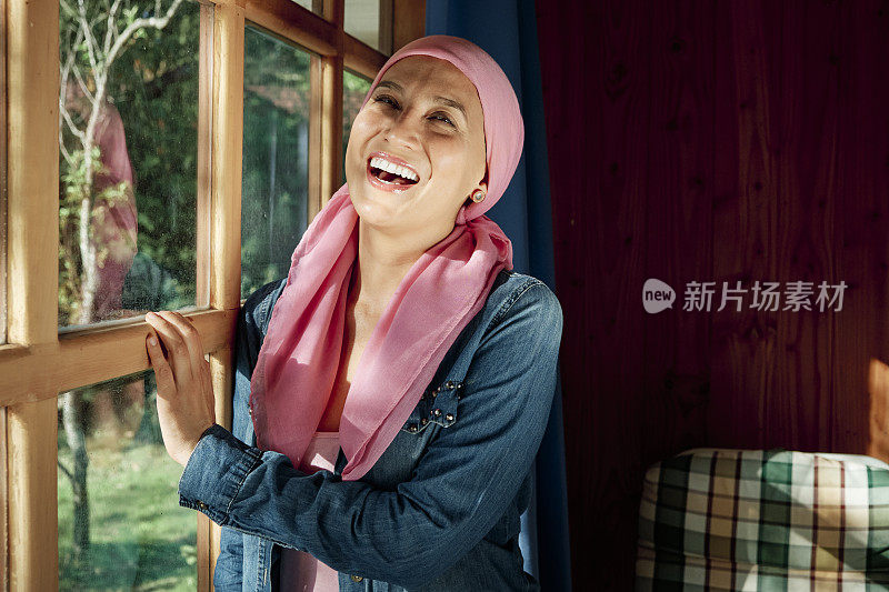 一位与癌症抗争的妇女在窗边大笑。