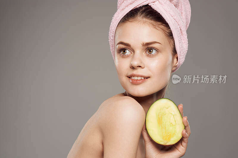 微笑的女人裸露着肩膀，头上裹着毛巾，手里拿着芒果