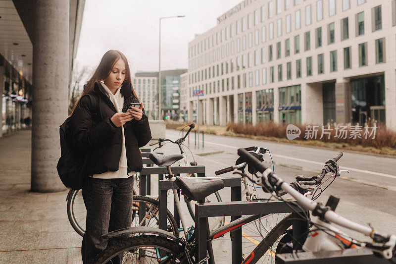 学龄女孩用智能手机租用电动滑板车或自行车，通过移动应用程序进行非接触式支付。秋冬季节的城市自行车租赁