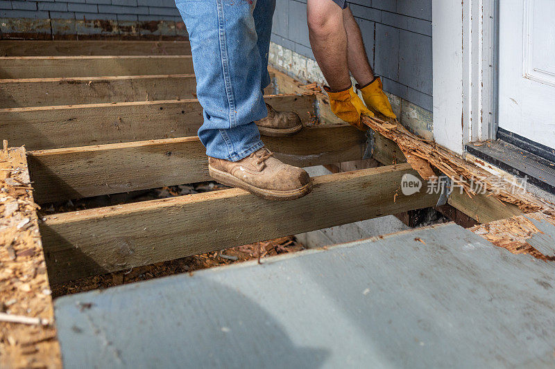 工人站在腐烂甲板的托梁上清除腐烂的木头