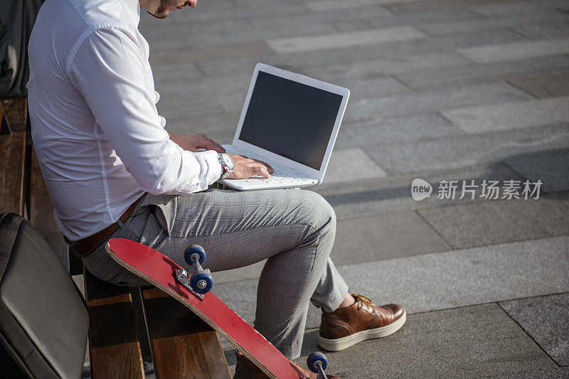有型胡须的男人用笔记本电脑和坐在长椅上拿着包在城市里