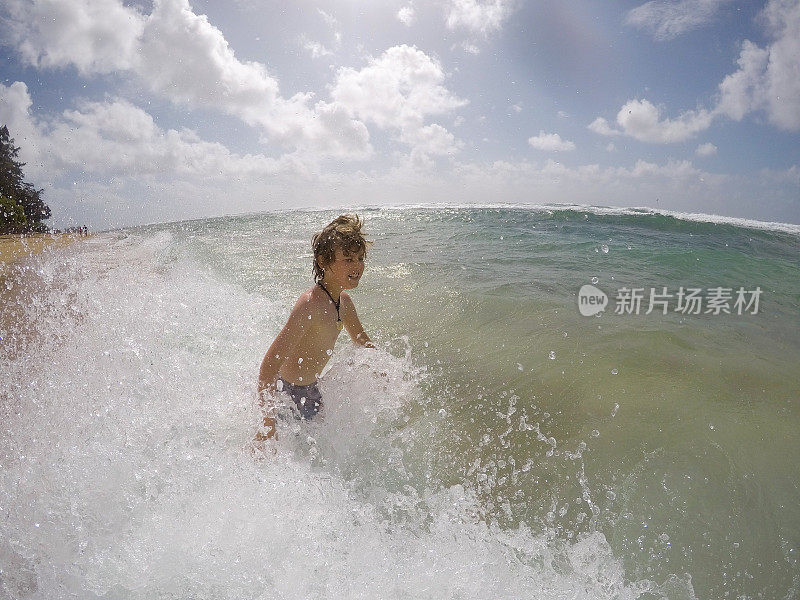 小男孩在夏威夷考艾岛玩，溅水，享受美丽的海水。