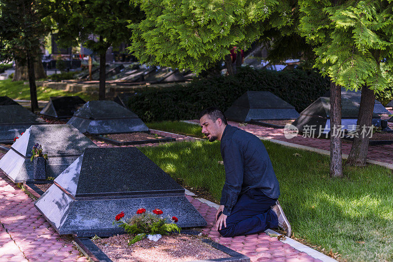 情绪紧张的黑衣男子跪在他已故朋友的墓前