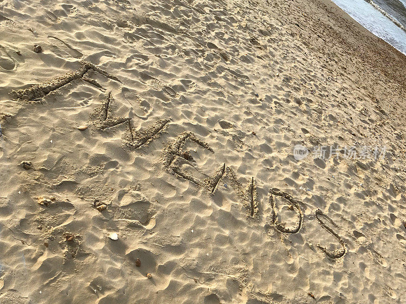 在阳光明媚的海滩上用木棍写在沙子上的单词，海浪，概念社交媒体照片在柔软的金色沙滩上书写字母，多塞特，英国海边的海岸线