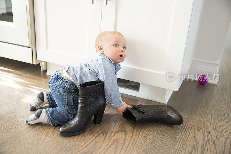小男孩在地板上玩他妈妈的靴子