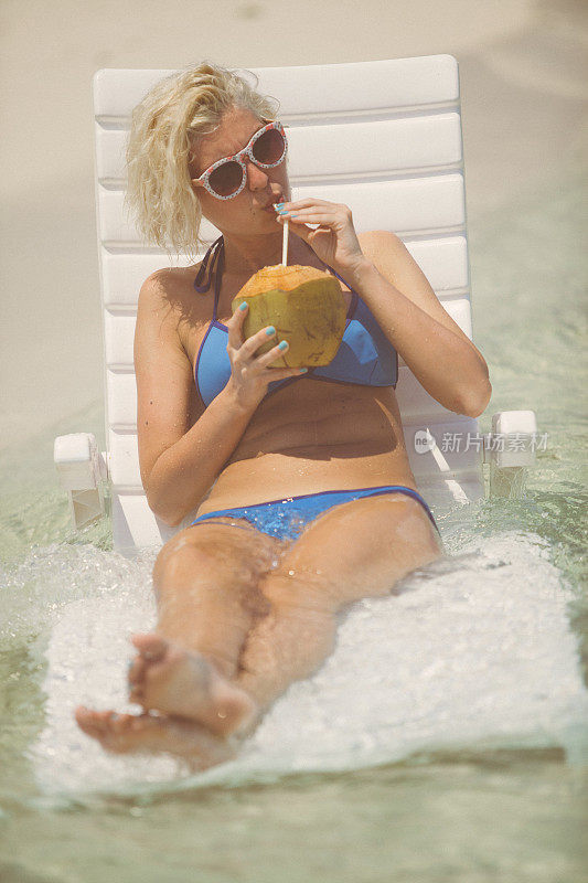 迷人的金发女人坐在和日光浴在浅水，马尔代夫