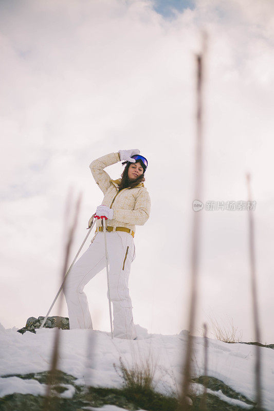 近景美丽的年轻女子在冬天的衣服站在一边，手拿木棍的背景雪山